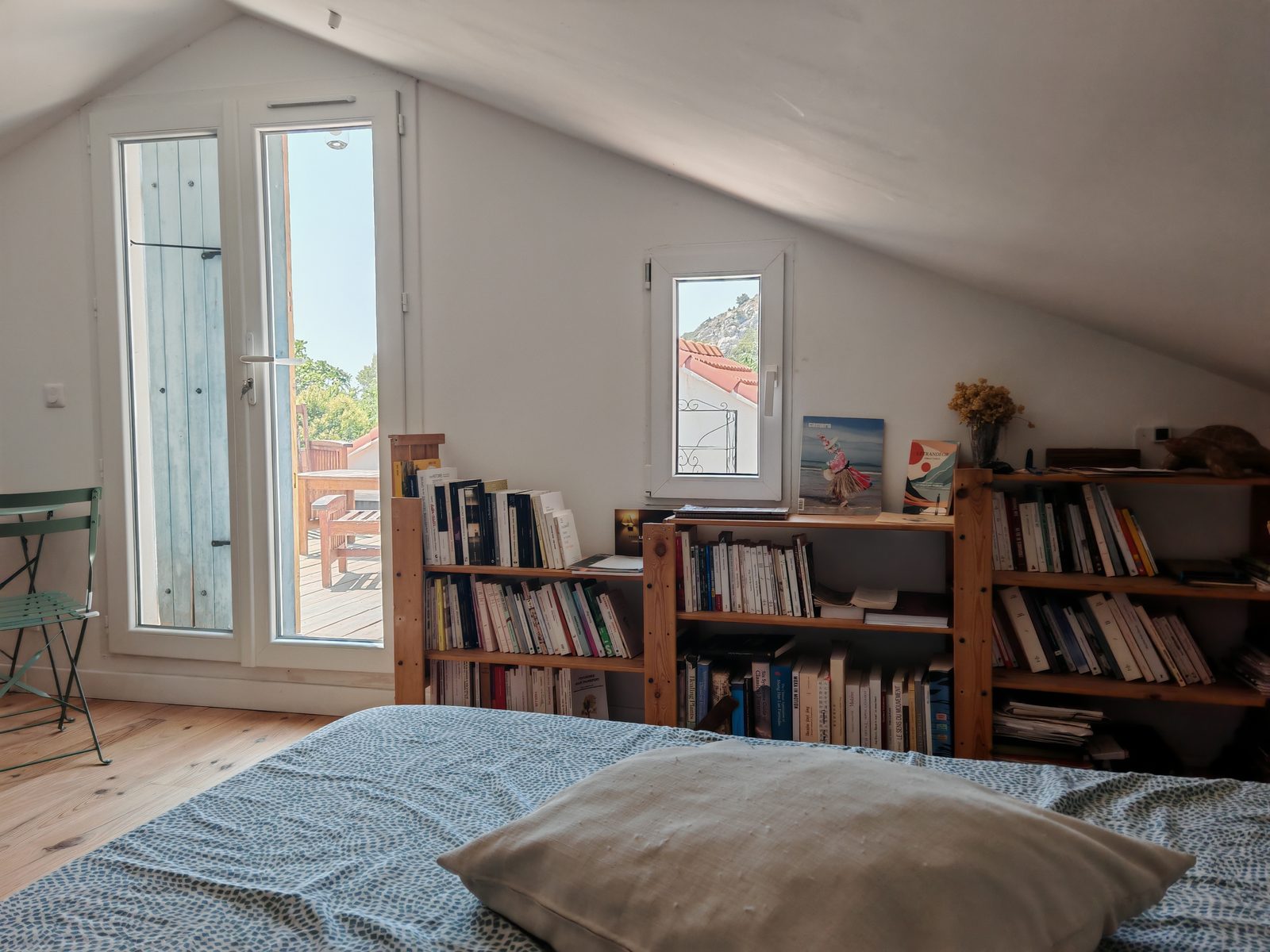 La chambre sous les toits de la Cabane : le lit, la bibliothèque et la porte-fenêtre ouverte sur la terrasse