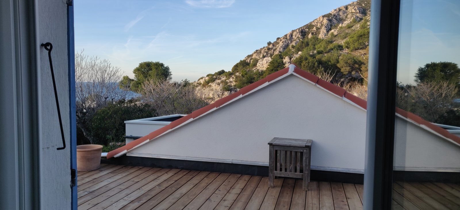 La porte de la Cabane ouverte sur le toit-terrasse et les collines, en fin de journée