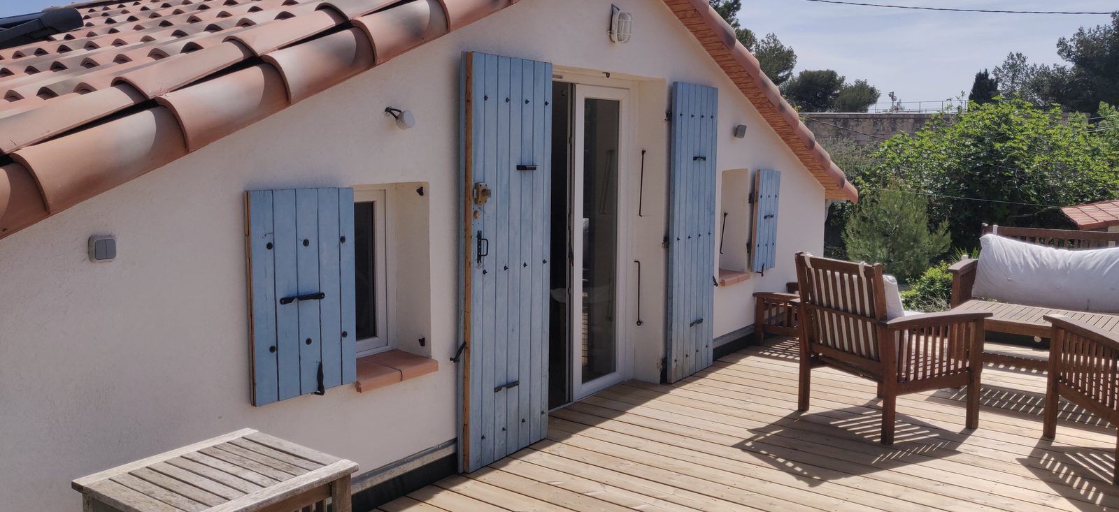 Les volets bleus de la chambre ouverts sur le toit-terrasse en bois